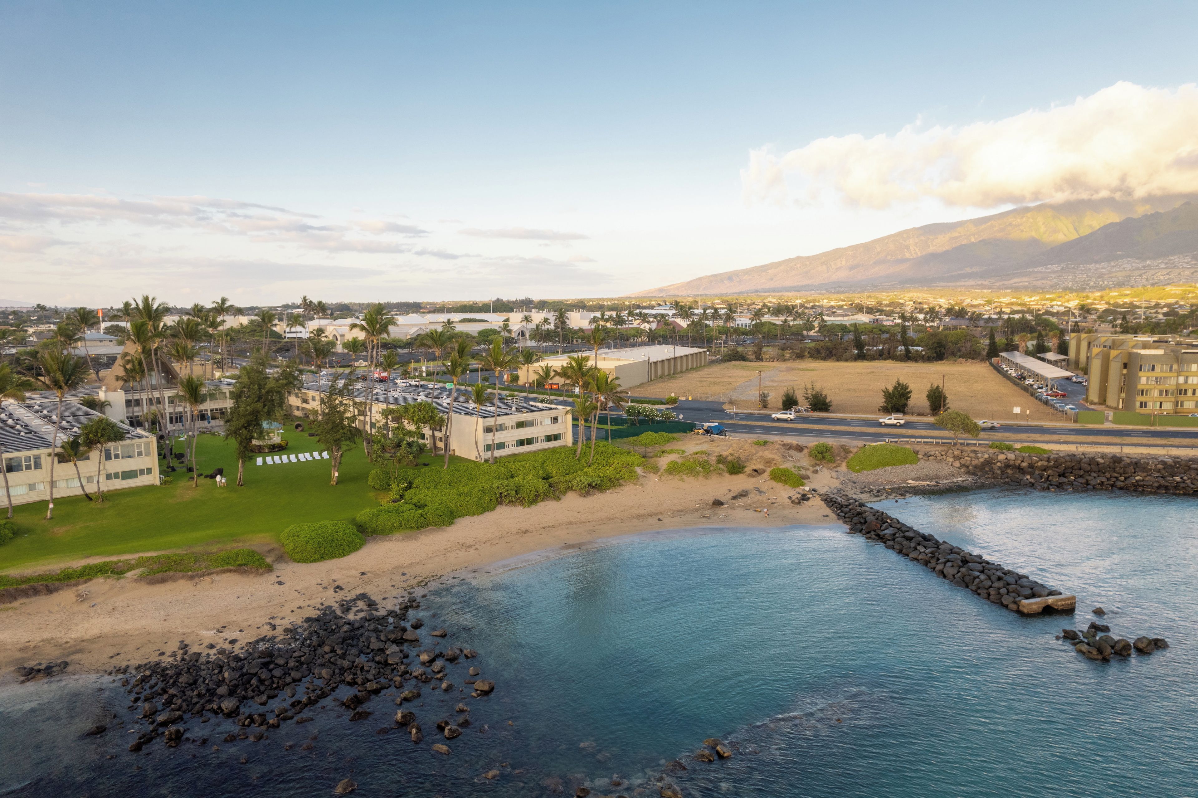 A coastal resort with a beachfront, palm trees, and a view of a mountain range.