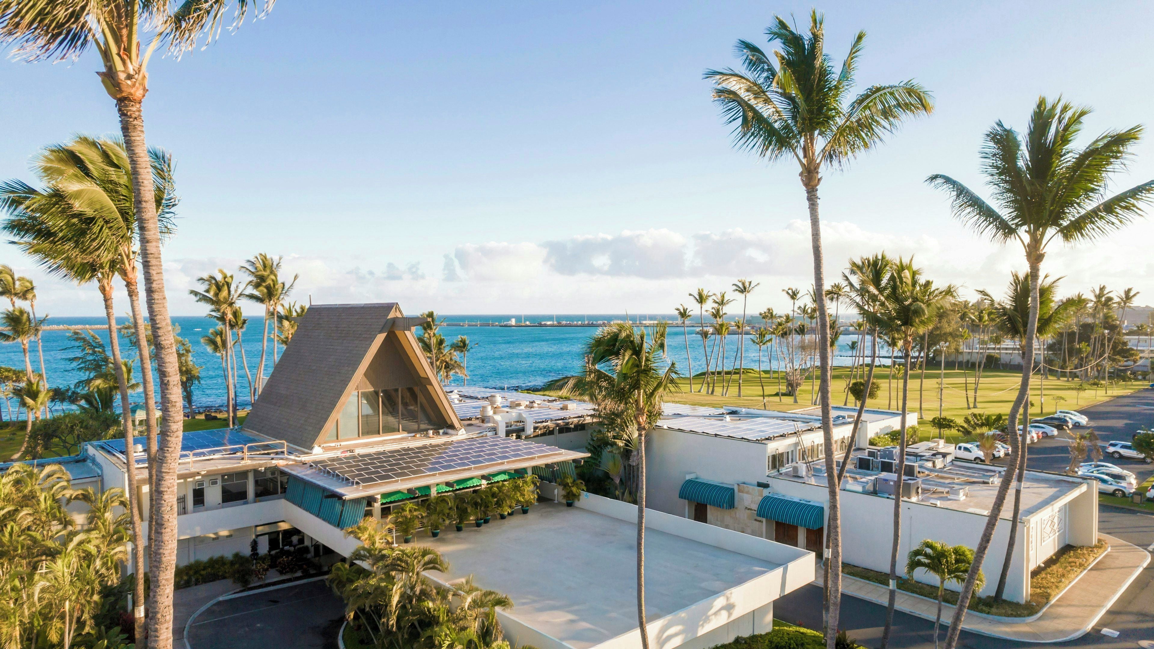 A resort with a beach view, palm trees, and a building with solar panels.