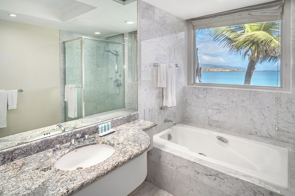 A modern bathroom with a marble sink, a bathtub, and a glass-enclosed shower.