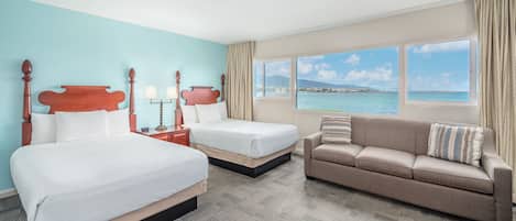 A hotel room with two beds, a sofa, and a large window offering a view of the sea.