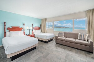 Habitación de hotel con dos camas, un sofá y un ventanal con vista al mar.