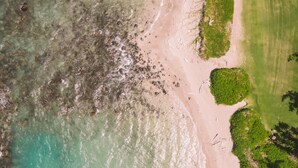 An aerial view of a beach with clear turquoise water, a sandy shore, and patches of green vegetation. - Maui Beach Hotel (Kahului)