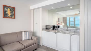 A hotel room with a sofa, a microwave, a coffee maker, and a view of the ocean.