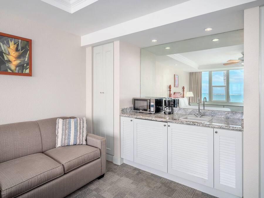 A hotel room with a sofa, a microwave, a coffee maker, and a view of the ocean.