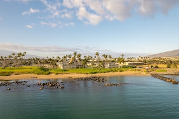 A large building with multiple floors, surrounded by palm trees and a beach. at Maui Beach Hotel