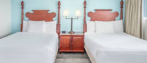 Une chambre d’hôtel avec deux lits simples, une table de chevet avec une lampe et une fenêtre avec des rideaux.