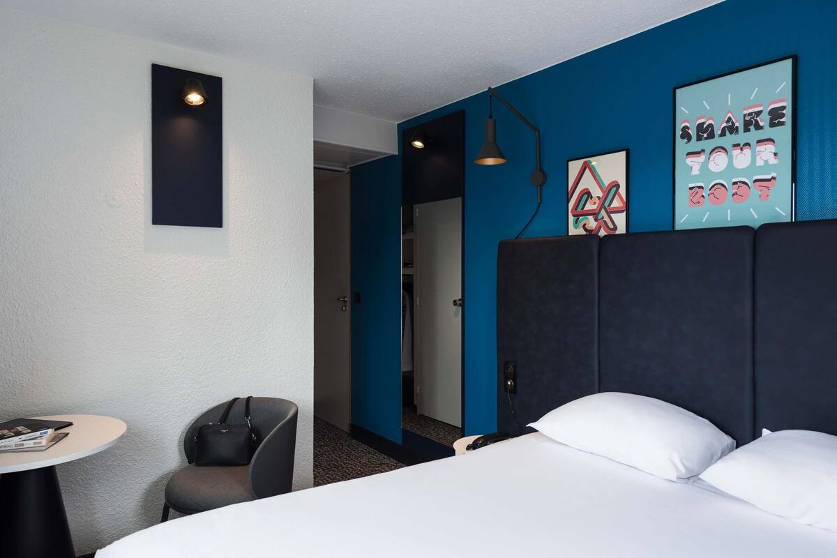 Een hotelkamer met een bed, een bureau, een stoel en een deur naar een badkamer.