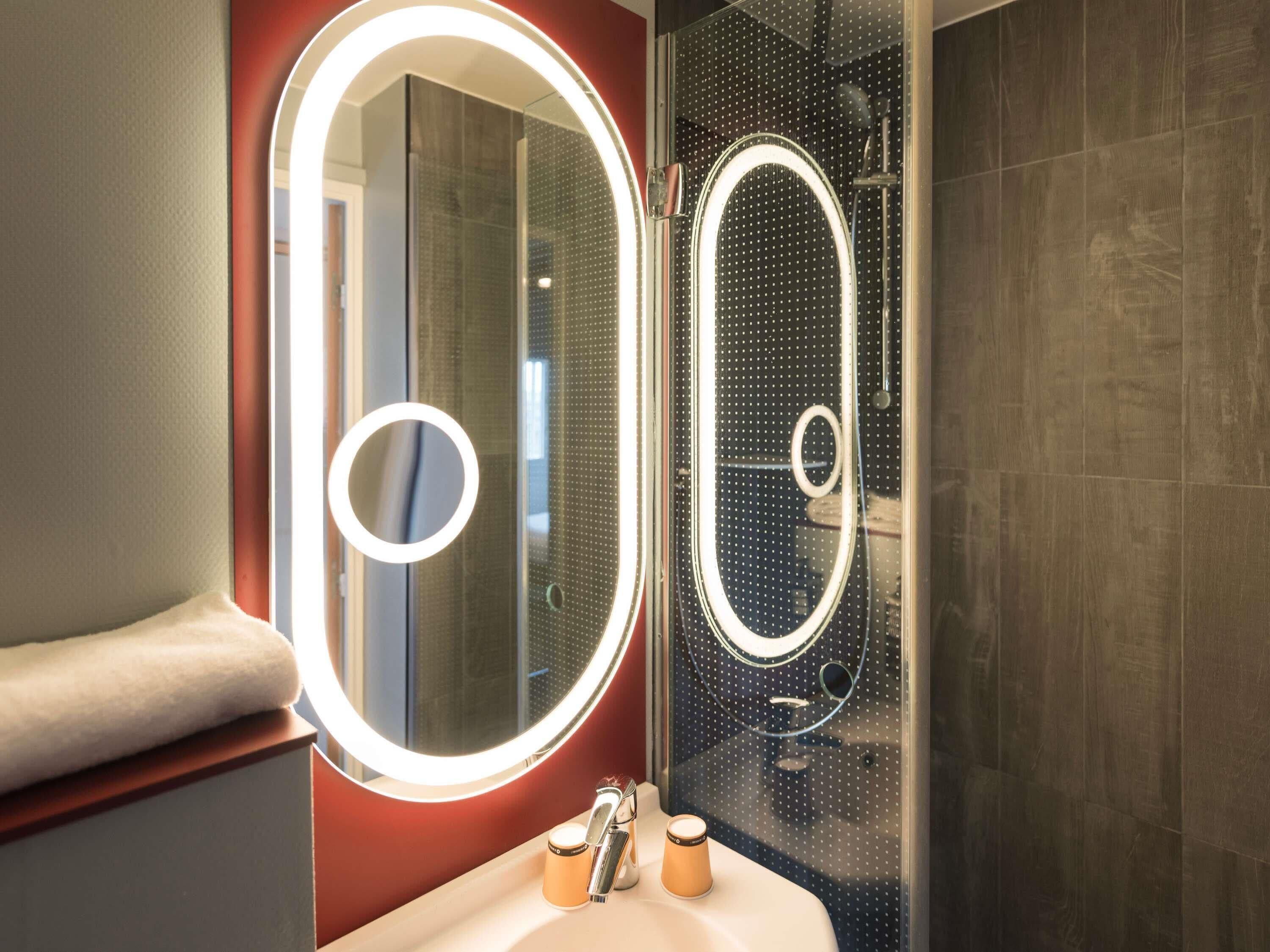 A bathroom with a vanity, a mirror with a light, and a shower area.