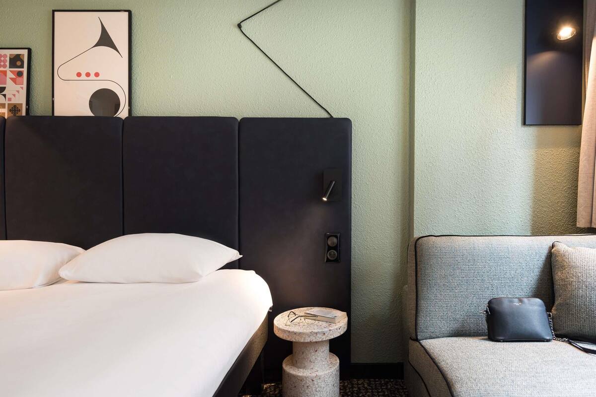 Een hotelkamer met een bed, een klein rond tafeltje, een bank en een wandlamp.
