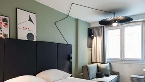 Hotelkamer met een groot bed, een bureau met stoel, een raam met gordijnen en een bijzondere lamp.