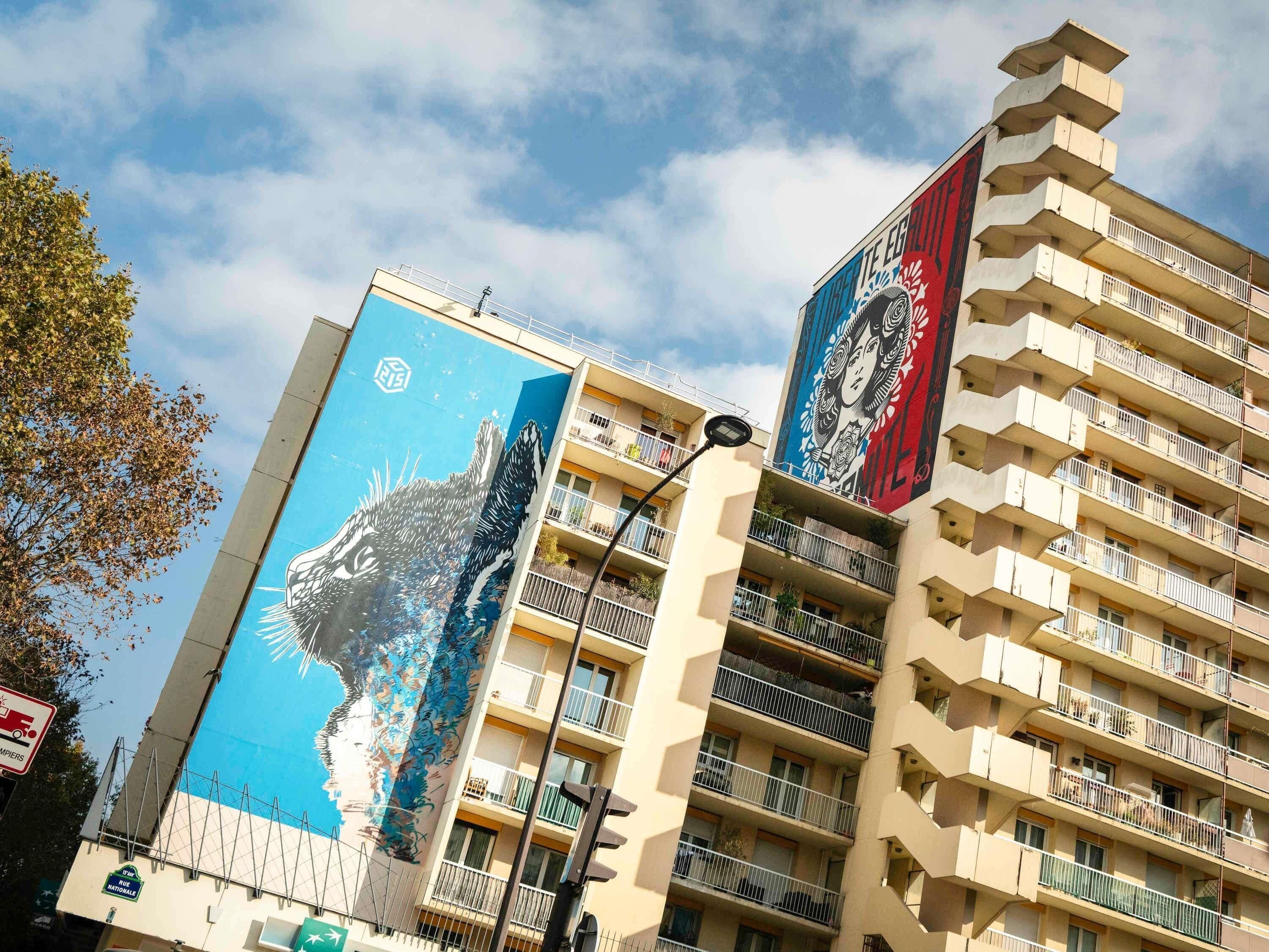 A multi-story building with balconies, a mural on the side, and a clear sky.
