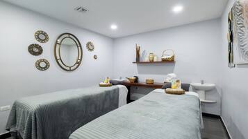 Two single beds with grey bedding, a nightstand, and a sink with a mirror.