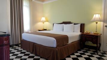 Una habitación de hotel con suelo a cuadros, cama con ropa de cama blanca y marrón, dos lámparas de noche, una mesita de noche de madera y un escritorio con teléfono.