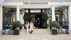 De ingang van hotel The Kensington, met een statig gevel, kolommen en potplanten.