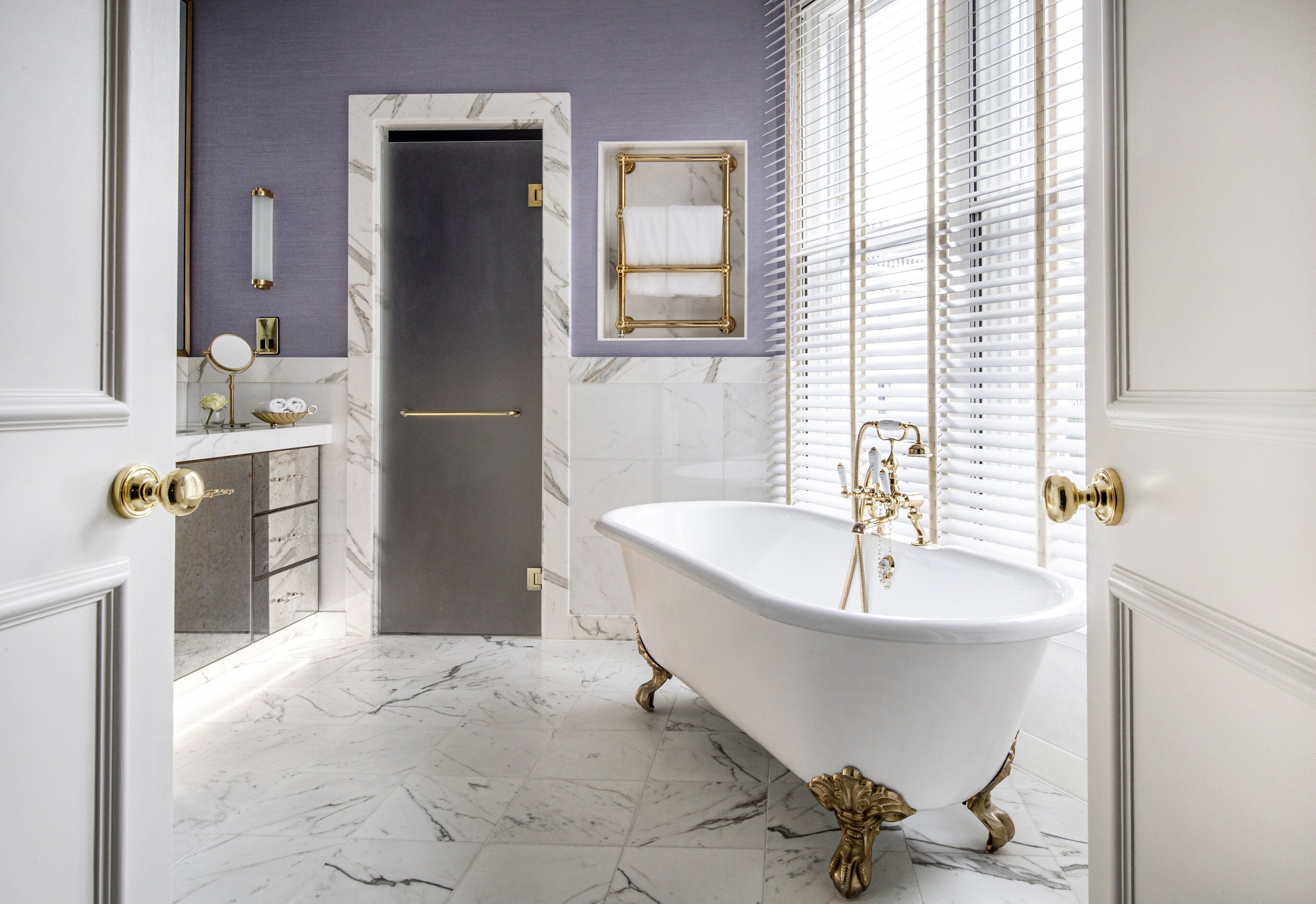 A bathroom with a freestanding bathtub, marble flooring, a vanity with a mirror, and a towel rack.