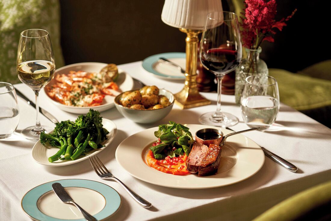 A dining table with plates of food, wine glasses, and cutlery.