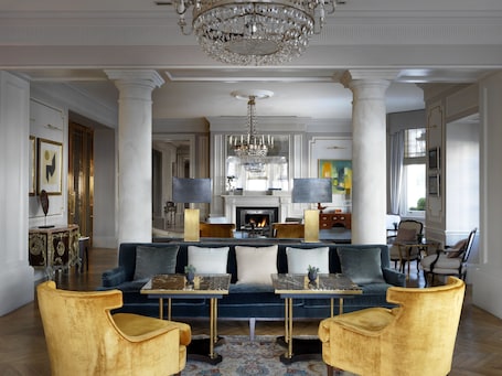 A spacious living room with a blue sofa, gold armchairs, a marble coffee table, and a large chandelier.