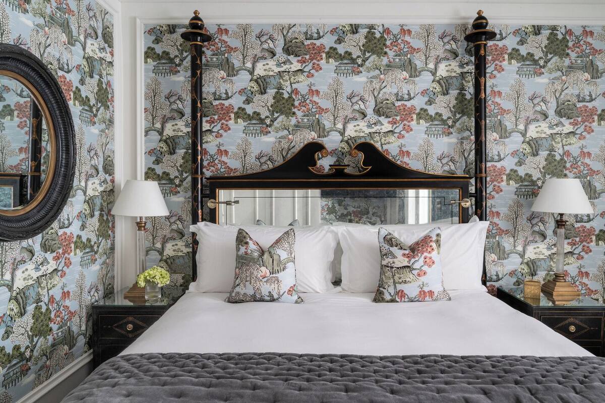 A bedroom with a four-poster bed, floral wallpaper, and two bedside tables with lamps.