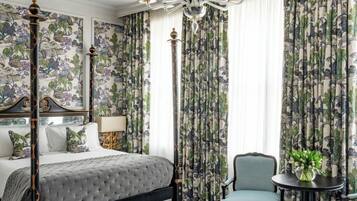 A bedroom with a four-poster bed, floral wallpaper, a chandelier, and a small round table with a plant.