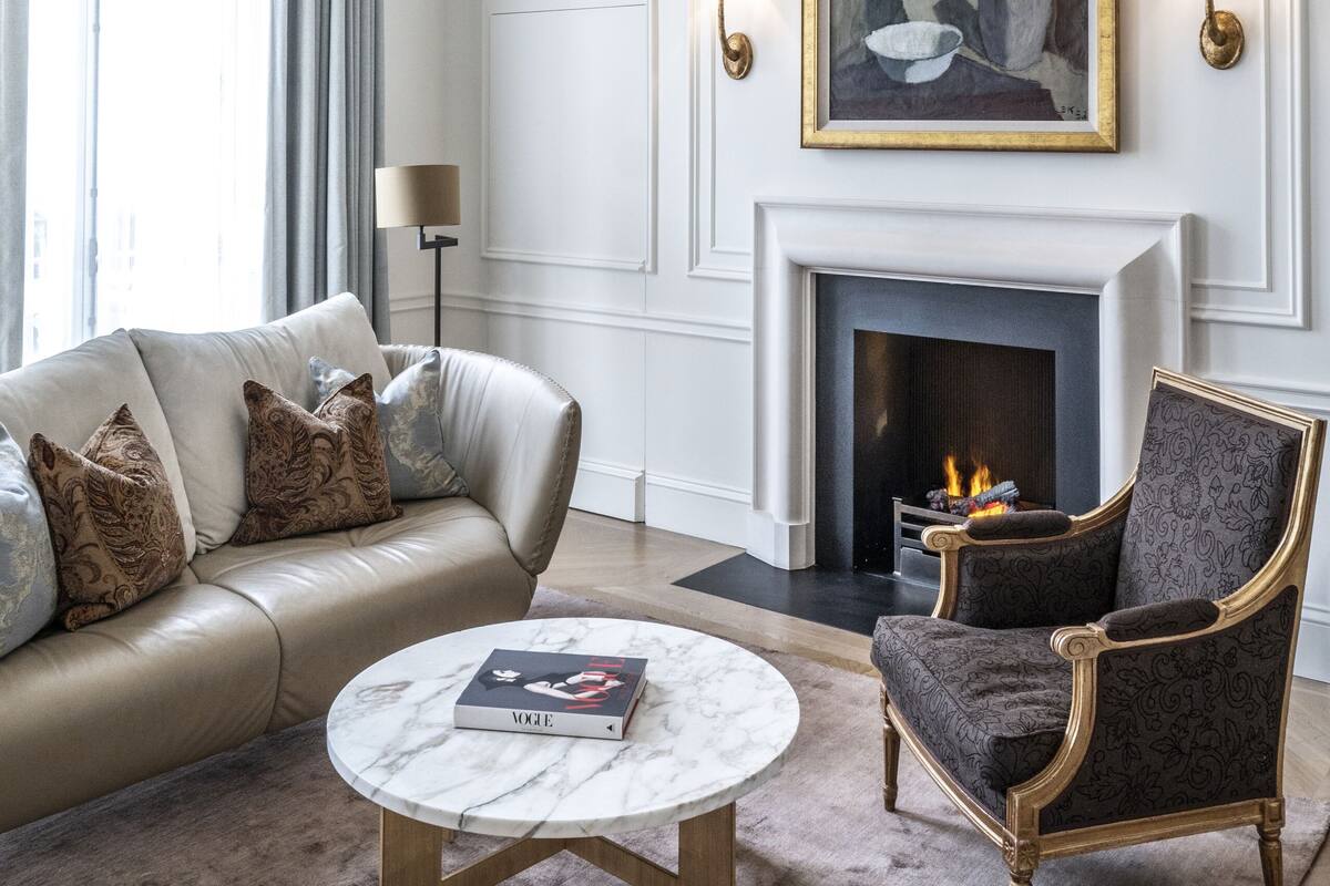 A living room with a beige sofa, a round coffee table, a patterned armchair, a fireplace, and a chandelier.
