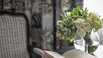 Ein offenes Buch auf einem schwarzen Tisch mit einem grünen Lesezeichen, eine Vase mit Blumen und ein Stuhl mit gemustertem Stoff.