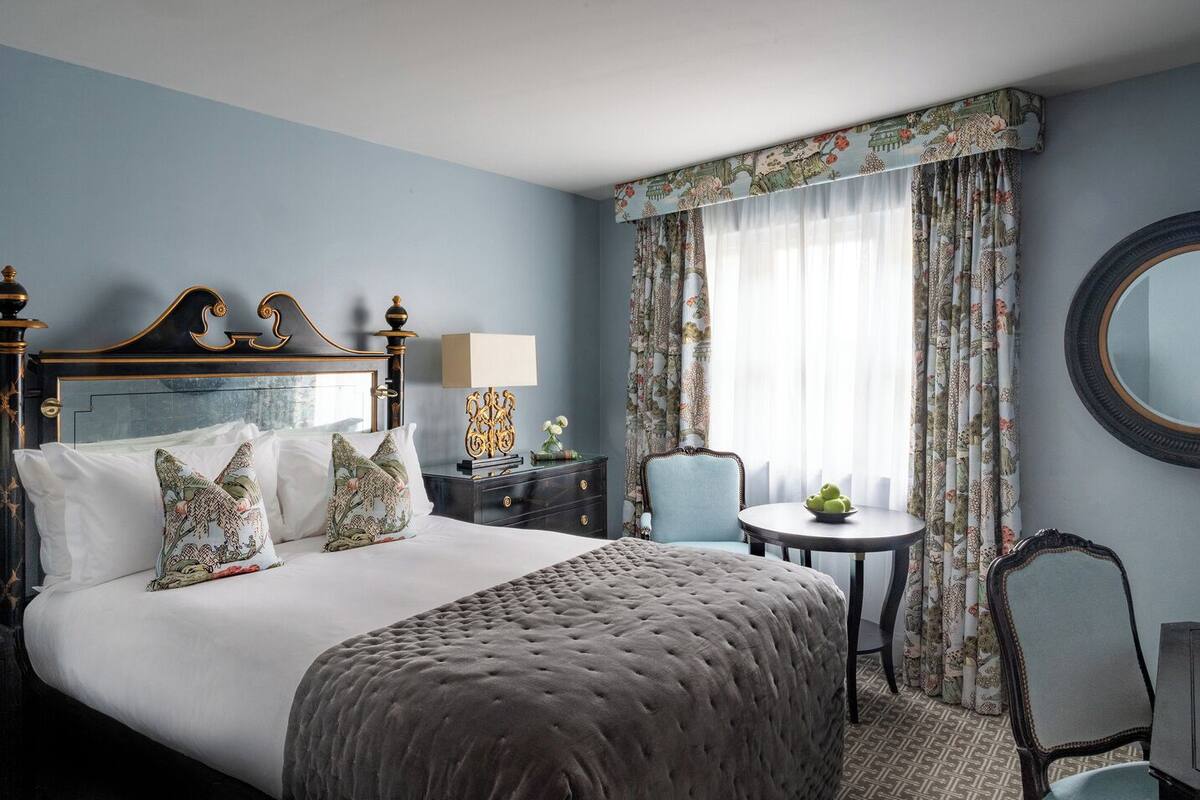 A hotel room with a large bed, a round table, a chair, and a mirror.
