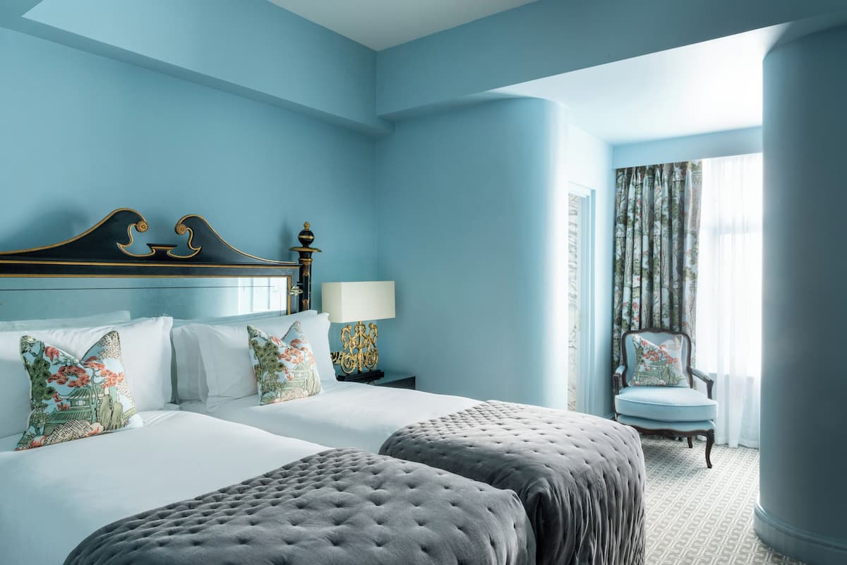 A hotel room with a large bed, two bedside tables, a chair, and a window with curtains.