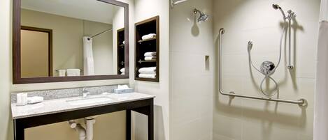 A modern bathroom with a dual sink vanity, a large mirror, a walk-in shower with a handheld showerhead, and a towel rack.