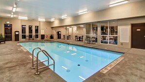 An indoor swimming pool with clear water, surrounded by a concrete floor and walls. There are multiple doors leading to other areas, and a few chairs and tables are visible near the pool. - Best Western London Airport Inn & Suites (London)