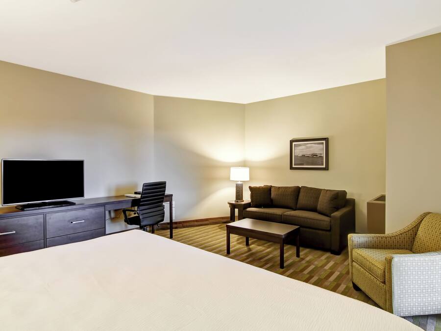 A hotel room with a bed, a desk with a TV, a sofa, a chair, and a lamp.