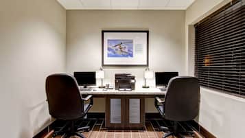 Una sala conferenze con un lungo tavolo, due sedie, due monitor, una stampante e un quadro incorniciato appeso al muro.