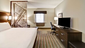 A hotel room with a bed, a desk with a TV, a chair, a window with curtains, and a patterned carpet. - Best Western London Airport Inn & Suites (London)