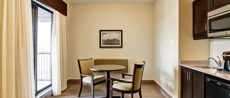 A dining area with a round table and two chairs, a kitchen with dark cabinets and a microwave, and a window with curtains.