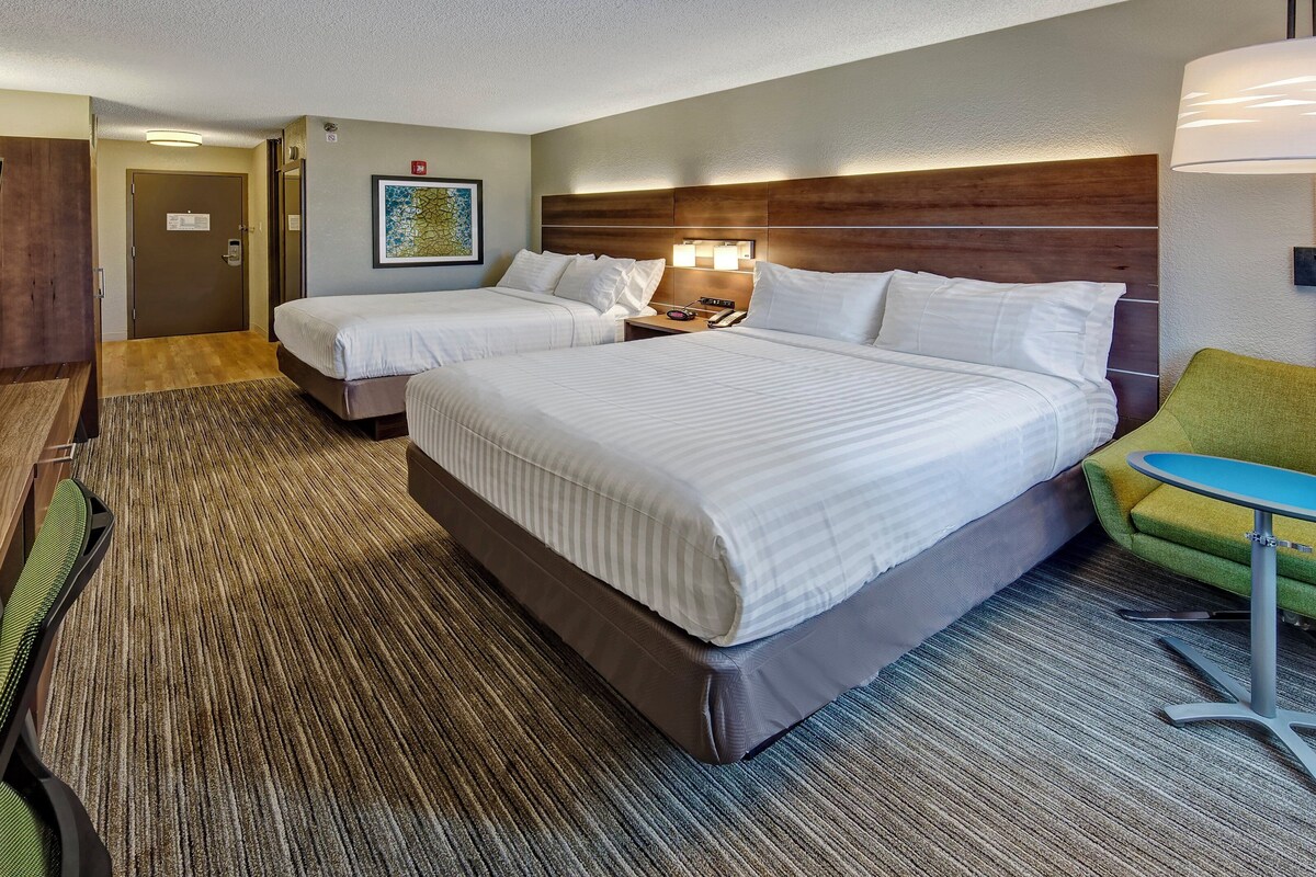 A hotel room with two beds, a TV, a desk, a chair, and a lamp.