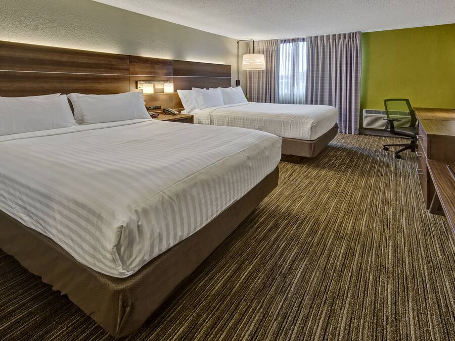 Une chambre d’hôtel avec deux lits, un bureau avec un ordinateur portable, une télévision et une grande fenêtre avec des rideaux.