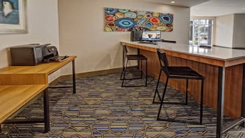 A hotel room with a wooden desk, two chairs, a computer, and a colorful abstract painting on the wall.