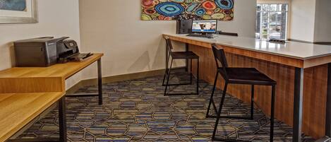 Habitación de hotel con un escritorio de madera, dos sillas, una computadora y un cuadro abstracto de colores en la pared.