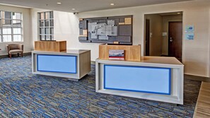 A reception area with two reception desks, a patterned carpet, and a wall-mounted sign. - Holiday Inn Express Louisville Airport Expo Center by IHG (Louisville)