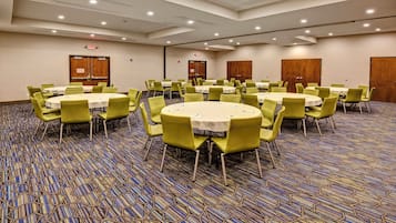 Un salón de conferencias con varias mesas y sillas, piso alfombrado y puertas.
