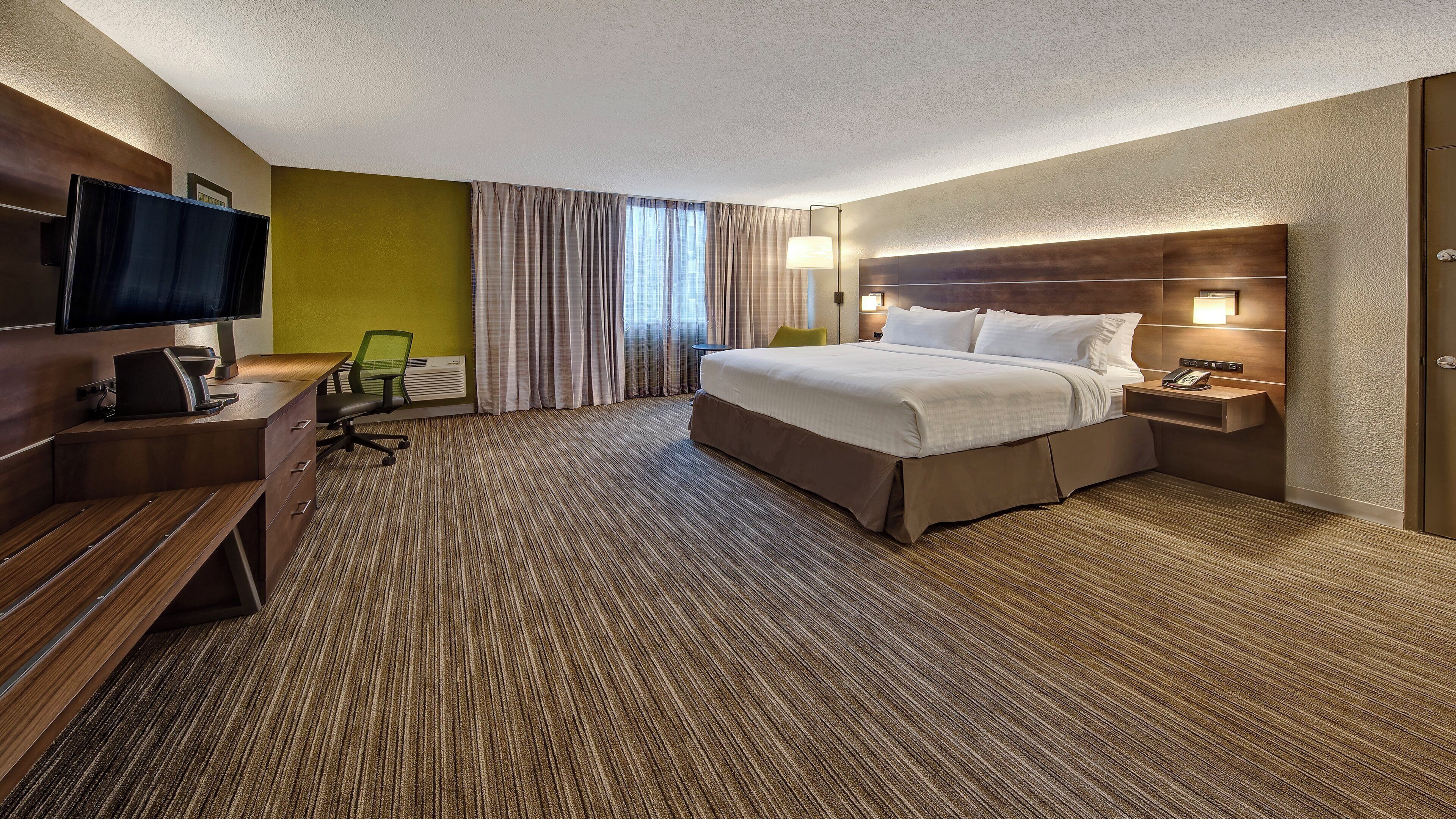 Ein Hotelzimmer mit Bett, Schreibtisch, Stuhl, Fernseher und einem Fenster mit Vorhängen.