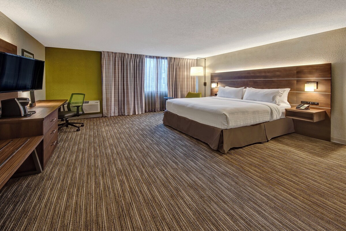 A hotel room with a bed, desk, chair, TV, and a window with curtains.