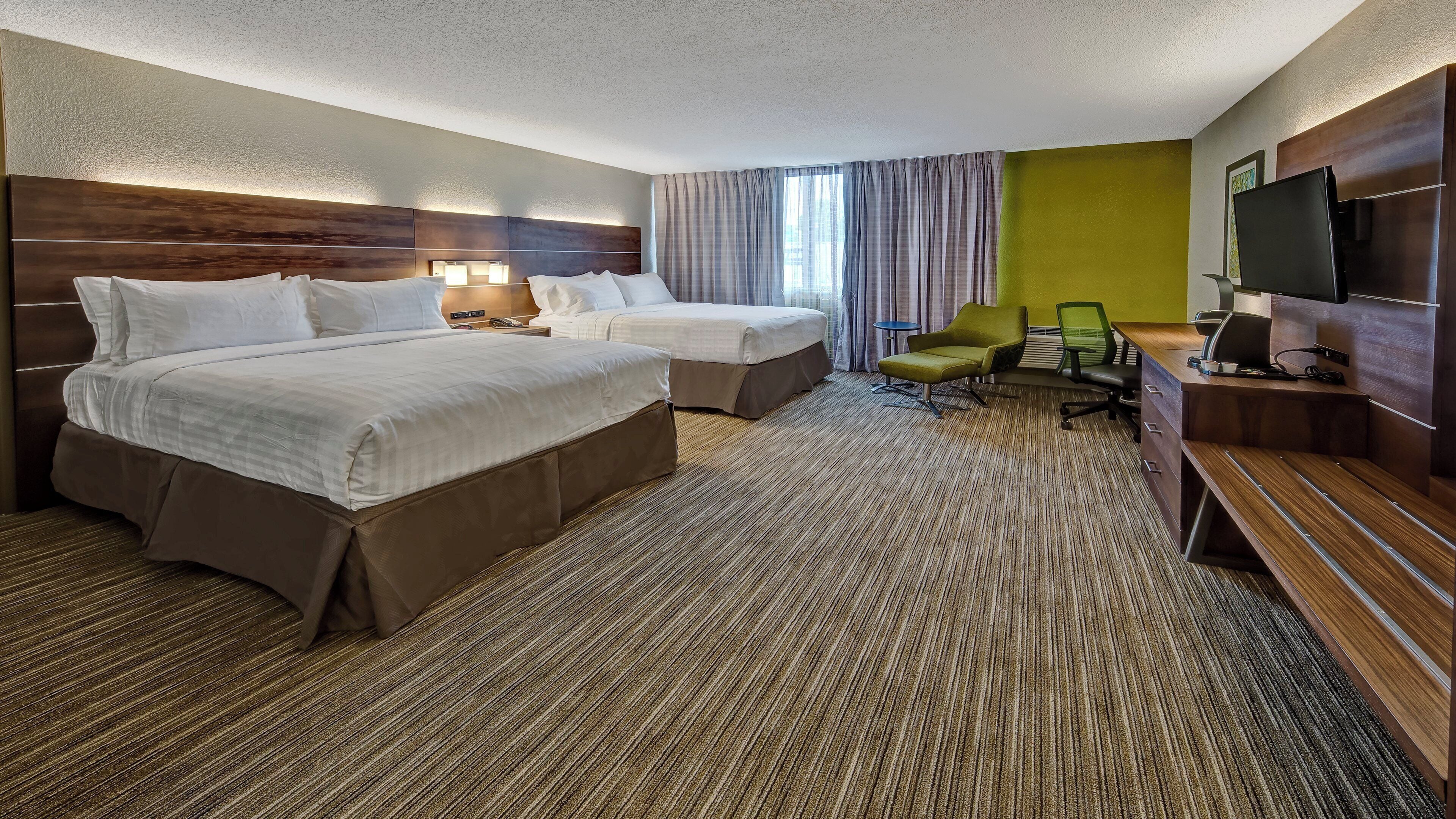 A hotel room with two beds, a desk, a chair, a television, and a large window with curtains.