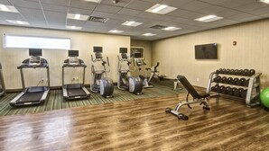 Un gimnasio con cintas de correr, elípticas, prensa de banca, mancuernas y una pelota de ejercicio verde.