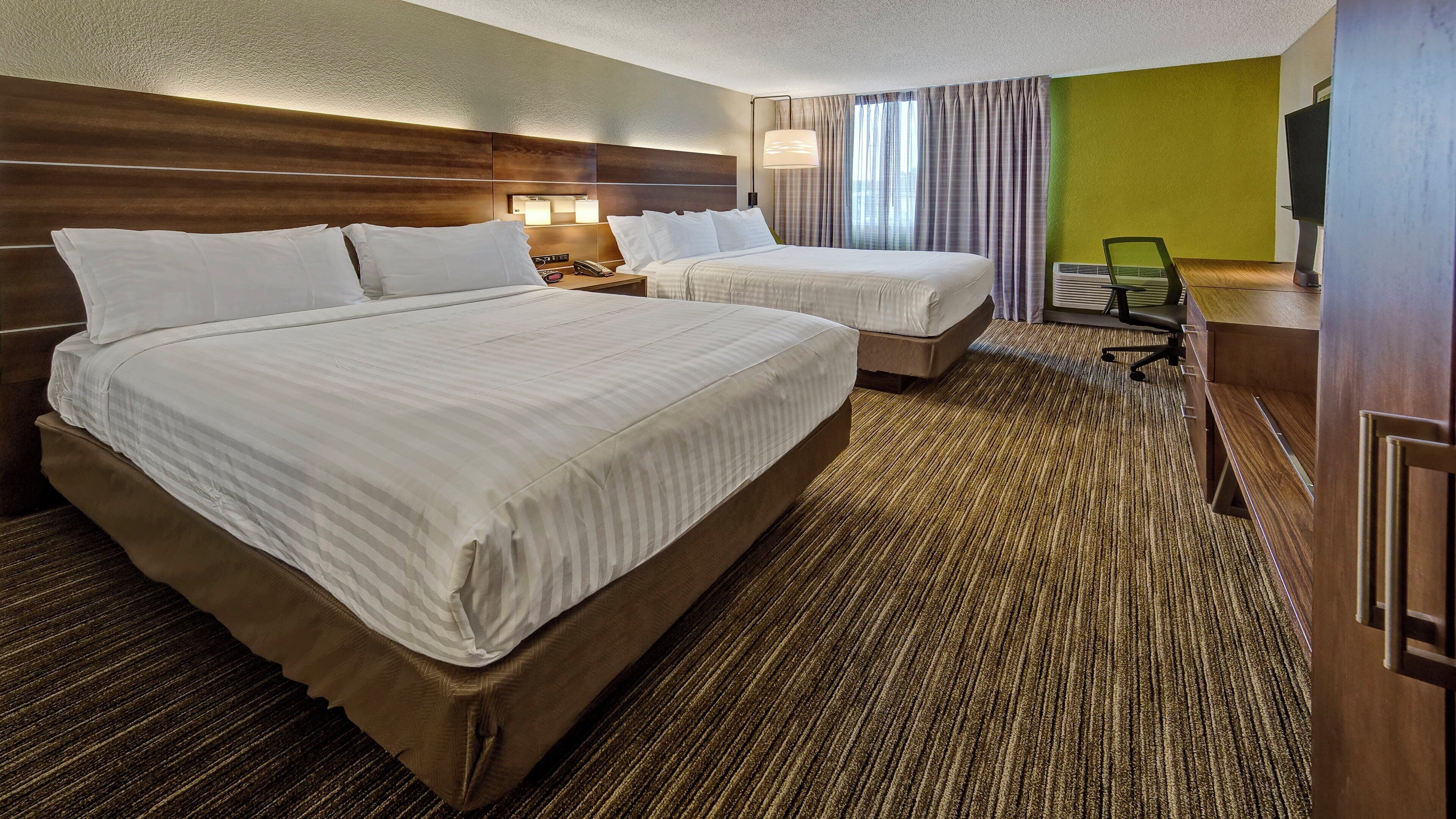 Habitación de hotel con dos camas, un escritorio con computadora, una silla y televisor.