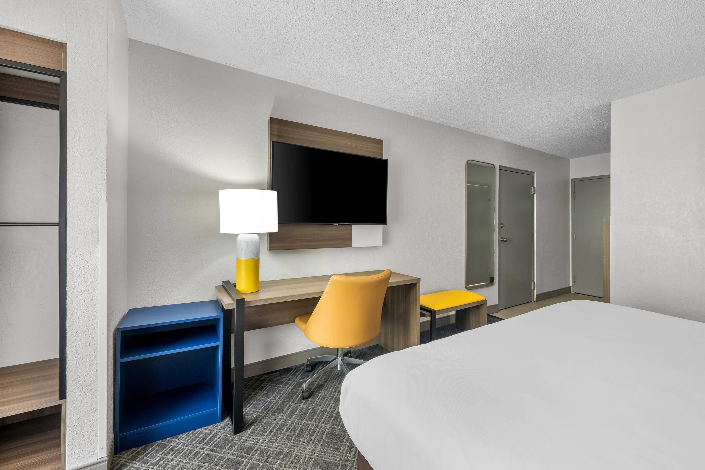 Una habitación de hotel con cama, escritorio con silla, televisión y armario.