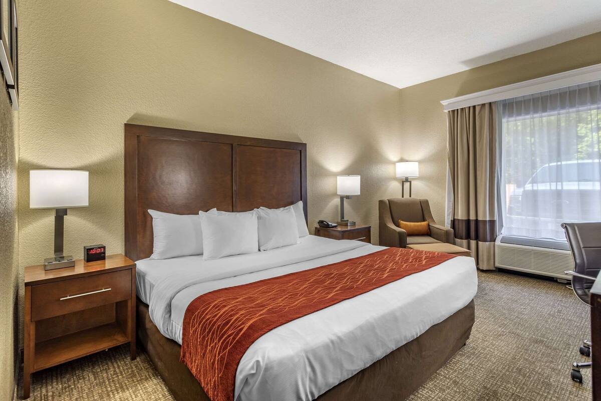 A hotel room with a large bed, two bedside tables with lamps, a chair, and a desk with a chair.