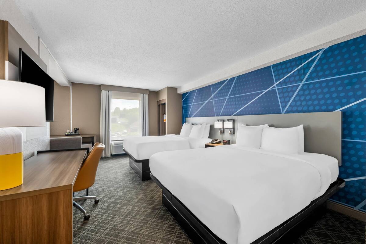 A hotel room with a large bed, a desk with a chair, a TV, and a window with curtains.