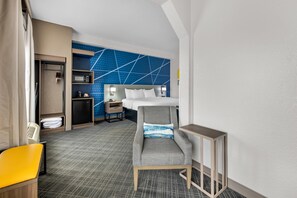Una habitación de hotel con cama, escritorio, silla, armario y microondas.