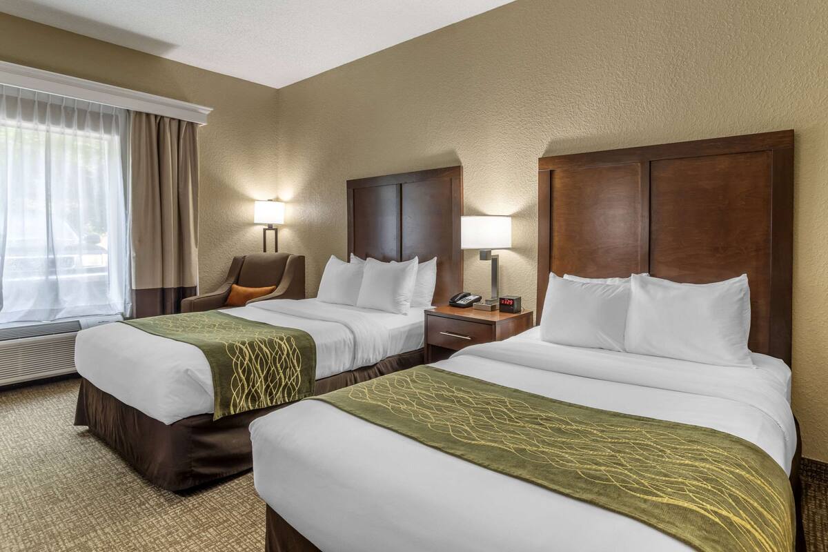 A hotel room with two beds, a chair, a desk, and a lamp.