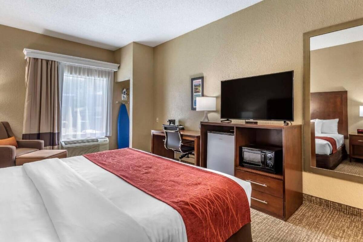 A hotel room with a bed, desk, chair, TV, and a mirror.
